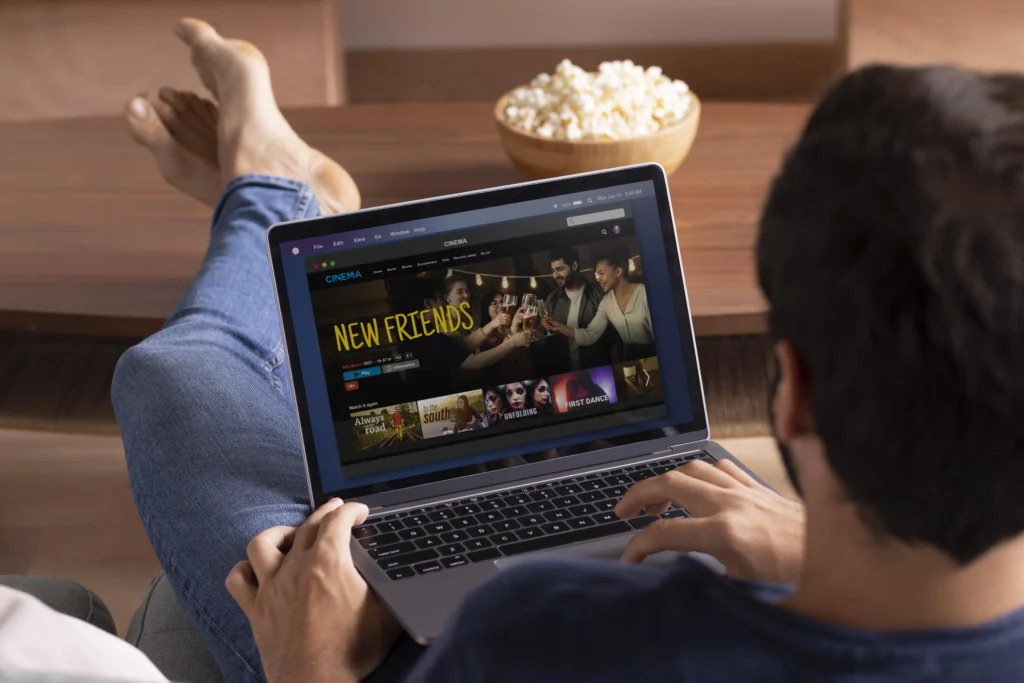 Person relaxing with a laptop browsing a movie streaming site, a bowl of popcorn beside them